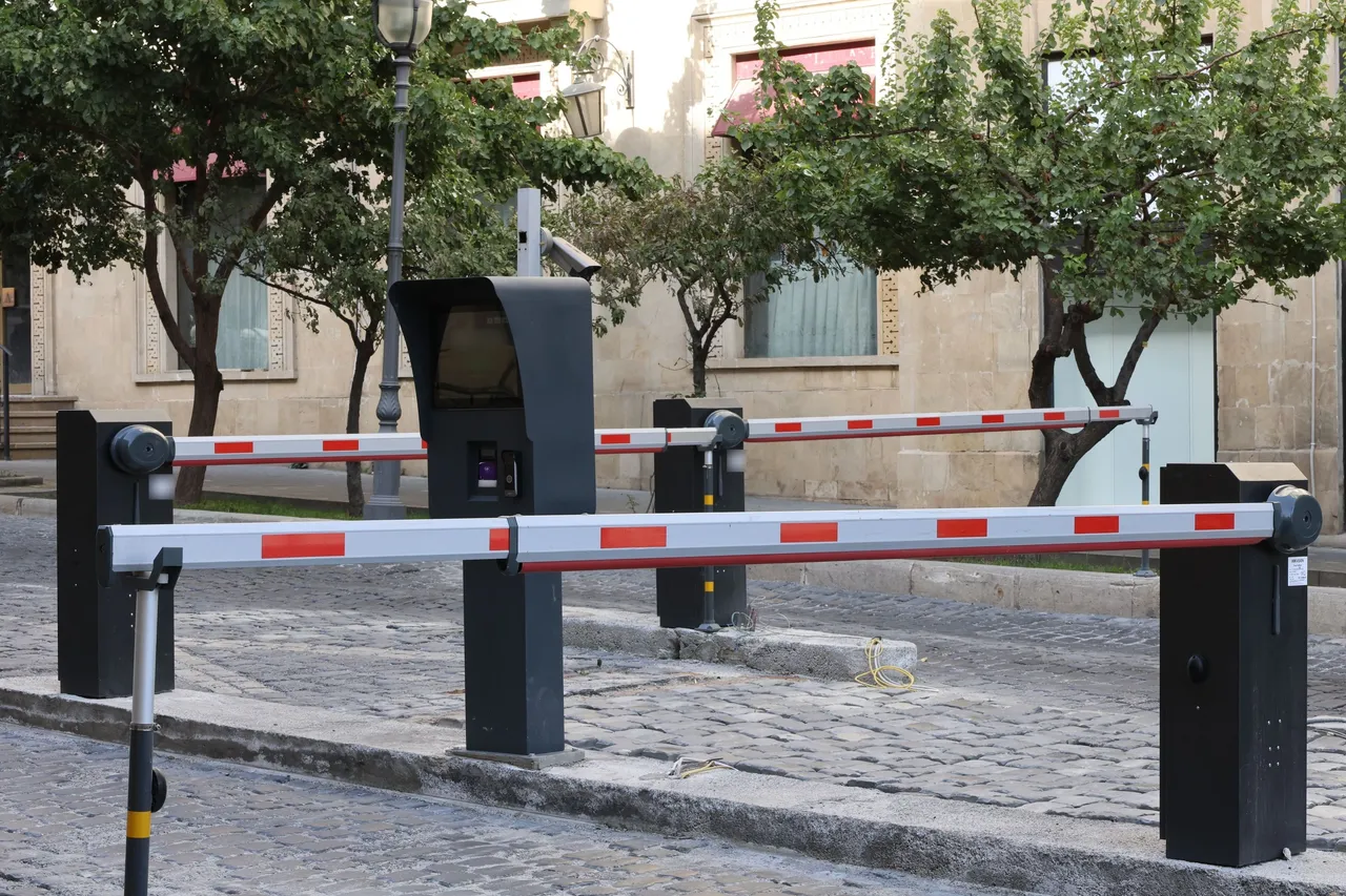 Arnavut kaldırımlı girişte iki kollu otomatik araç bariyeri ve kontrol kulesi